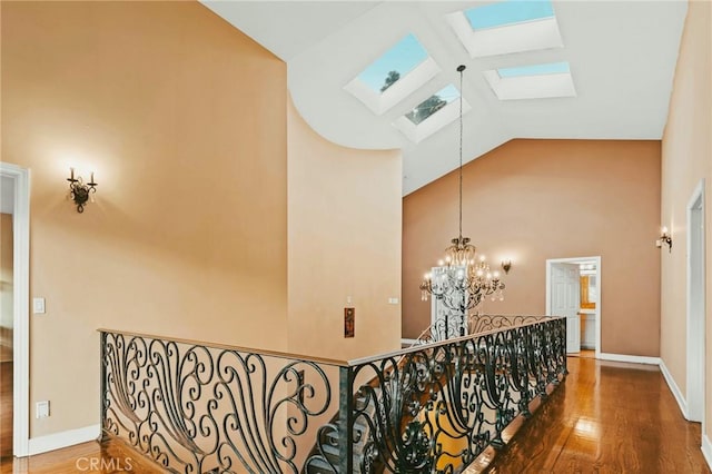 hallway with high vaulted ceiling, a skylight, dark hardwood / wood-style floors, and a notable chandelier