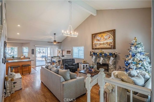 living room with hardwood / wood-style floors, a stone fireplace, high vaulted ceiling, ceiling fan with notable chandelier, and beamed ceiling