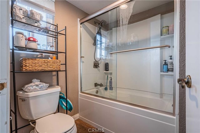 bathroom featuring toilet and bath / shower combo with glass door