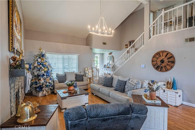 living room with an inviting chandelier, light hardwood / wood-style flooring, a stone fireplace, and high vaulted ceiling