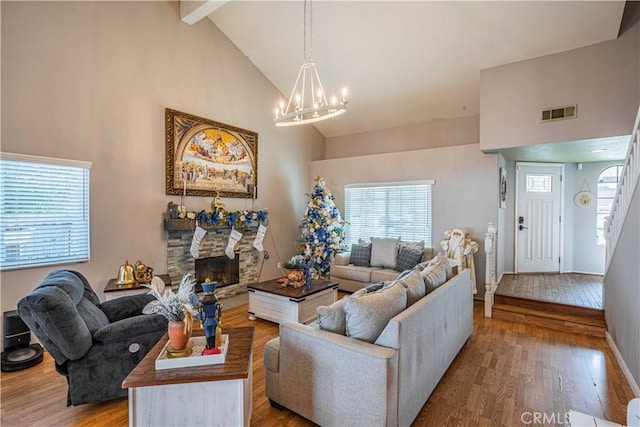 living room with hardwood / wood-style flooring, a stone fireplace, high vaulted ceiling, a chandelier, and beamed ceiling