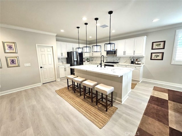 kitchen featuring decorative backsplash, white cabinetry, stainless steel appliances, and an island with sink