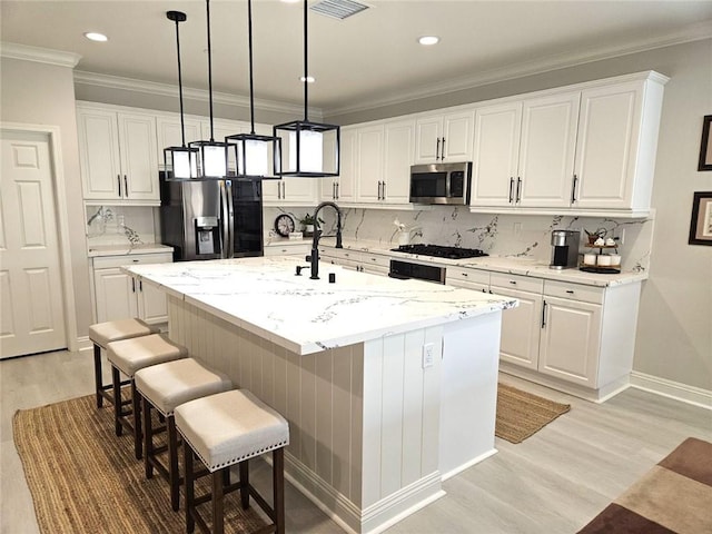 kitchen featuring light stone countertops, stainless steel appliances, white cabinets, and an island with sink