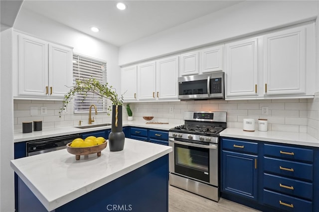 kitchen with white cabinetry, appliances with stainless steel finishes, blue cabinetry, sink, and a center island