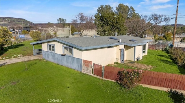 rear view of property featuring a yard, fence, and stucco siding