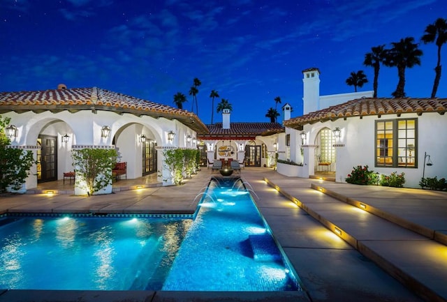 back house at twilight with pool water feature, french doors, and a patio