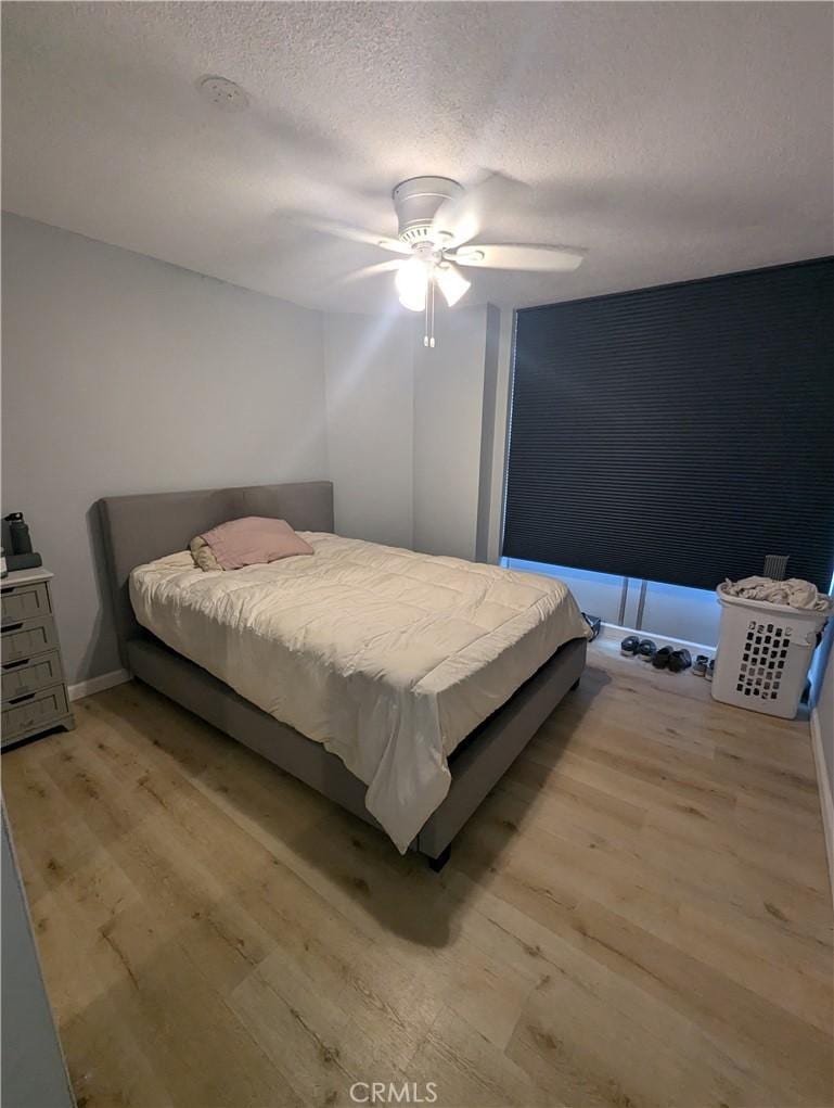 bedroom featuring light wood-type flooring, ceiling fan, and a textured ceiling