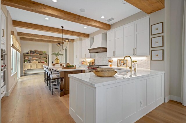 kitchen with custom exhaust hood, decorative light fixtures, white cabinetry, beamed ceiling, and kitchen peninsula