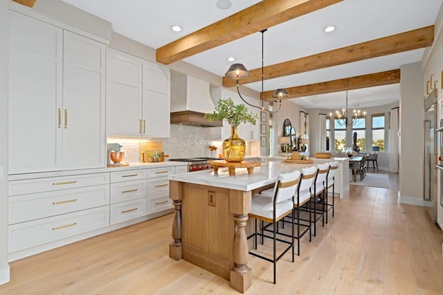 kitchen with white cabinets, custom exhaust hood, decorative light fixtures, decorative backsplash, and a large island