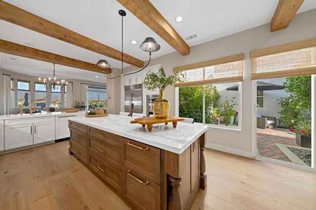 kitchen featuring pendant lighting, a center island, white cabinetry, stainless steel appliances, and light stone counters