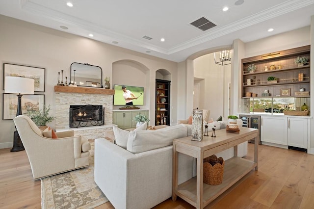 living room featuring light hardwood / wood-style floors, built in shelves, a raised ceiling, and a stone fireplace