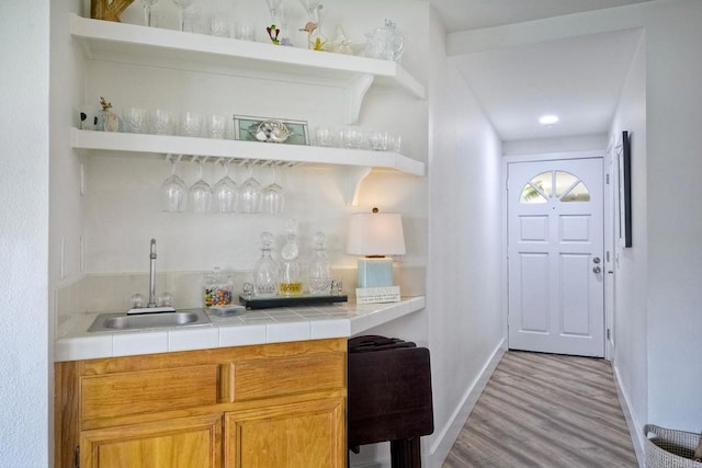 bar with tile countertops, light hardwood / wood-style floors, and sink