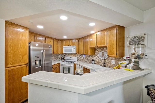 kitchen featuring white appliances, tile countertops, kitchen peninsula, and decorative backsplash