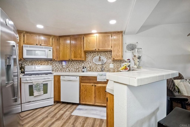 kitchen with tile countertops, kitchen peninsula, white appliances, light hardwood / wood-style floors, and backsplash