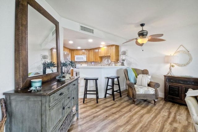 kitchen with a breakfast bar area, light wood-type flooring, kitchen peninsula, ceiling fan, and decorative backsplash