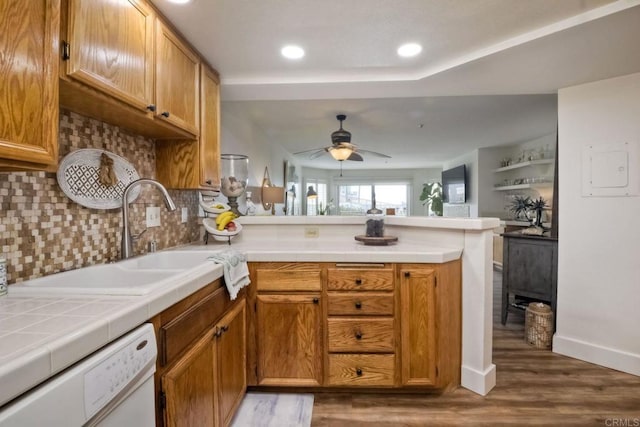 kitchen with sink, dark wood-type flooring, dishwasher, decorative backsplash, and kitchen peninsula