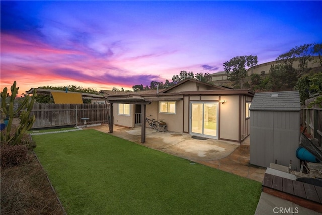 back house at dusk with a storage unit, a yard, and a patio