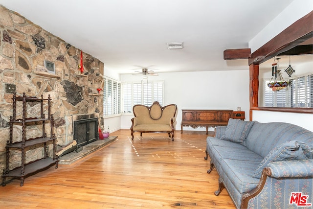 living room with a stone fireplace, ceiling fan with notable chandelier, and light hardwood / wood-style flooring