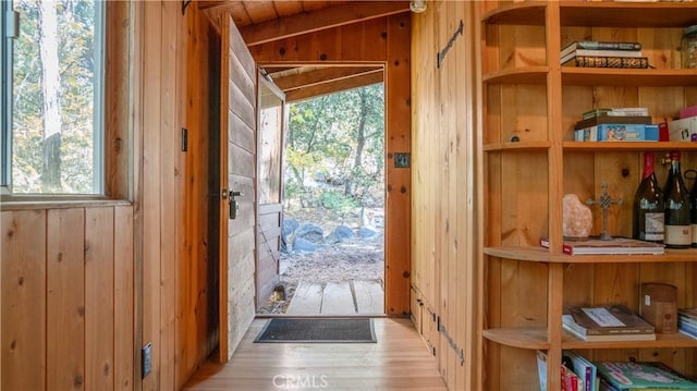 doorway to outside with plenty of natural light, light wood-type flooring, wooden walls, and vaulted ceiling