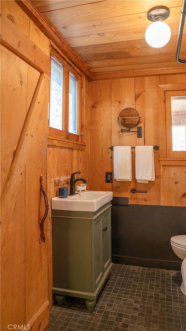 bathroom with toilet, wood walls, wood ceiling, and a healthy amount of sunlight