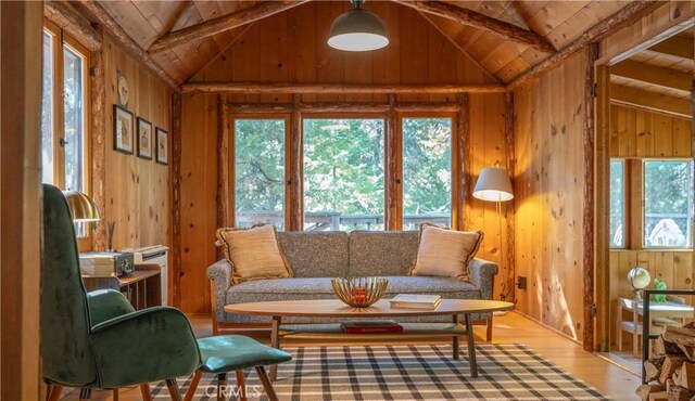 living room featuring a healthy amount of sunlight, lofted ceiling with beams, wood walls, and light hardwood / wood-style flooring