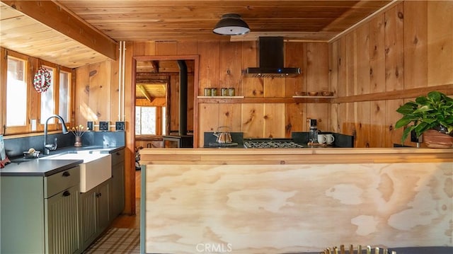 kitchen featuring wall chimney range hood, wooden walls, sink, wooden ceiling, and green cabinets