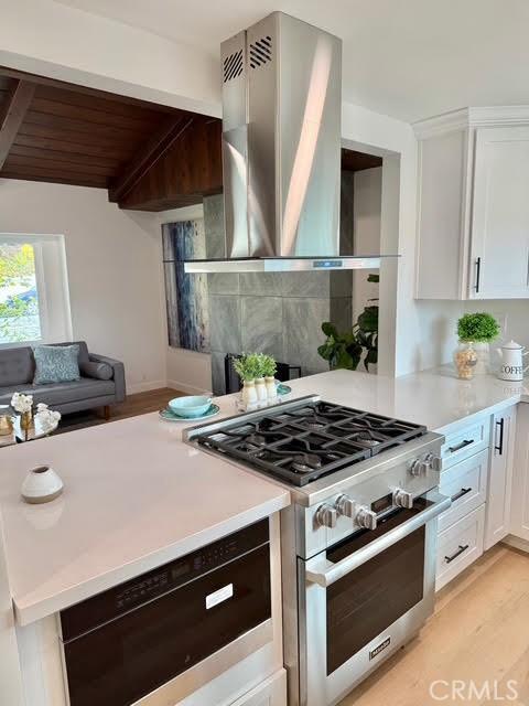 kitchen with wood ceiling, ventilation hood, light wood-type flooring, stainless steel stove, and white cabinets