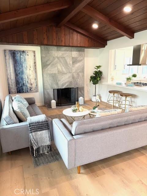 living room with light hardwood / wood-style floors, lofted ceiling with beams, wood ceiling, and a fireplace