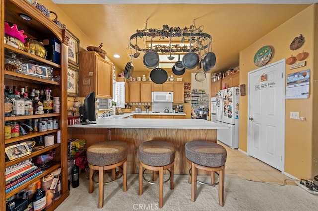 kitchen with a breakfast bar, white appliances, light tile patterned floors, and kitchen peninsula