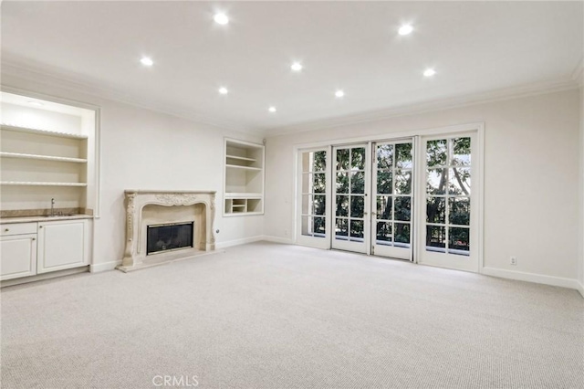 unfurnished living room featuring light colored carpet, a high end fireplace, crown molding, and built in features