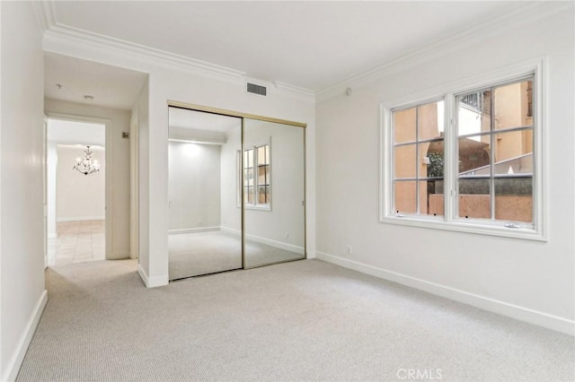 unfurnished bedroom featuring light colored carpet, a closet, crown molding, and a chandelier