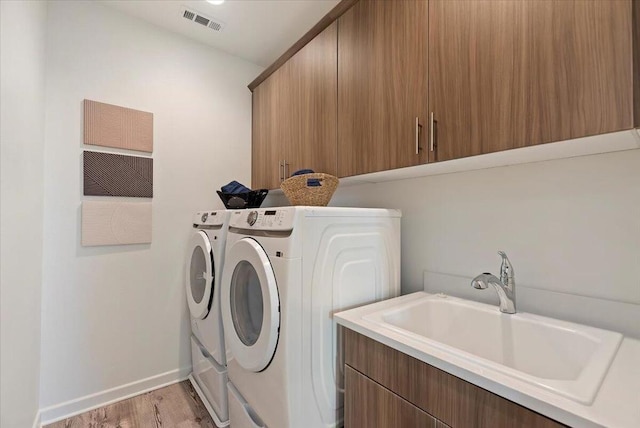 laundry room featuring independent washer and dryer, sink, light hardwood / wood-style floors, and cabinets