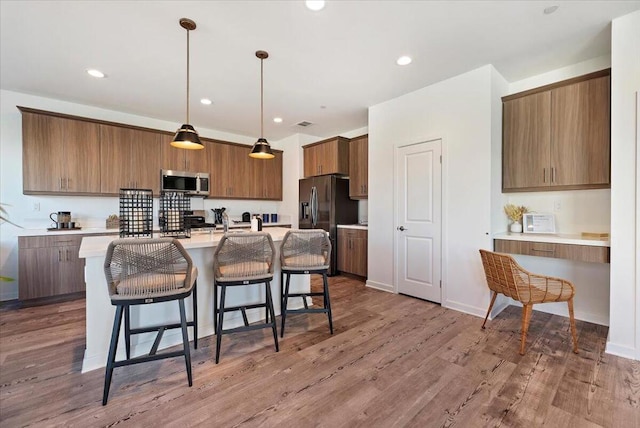 kitchen featuring pendant lighting, appliances with stainless steel finishes, hardwood / wood-style floors, an island with sink, and a breakfast bar area