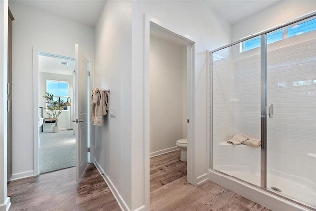 bathroom with toilet, a shower with shower door, and hardwood / wood-style flooring