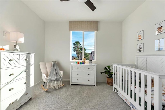 bedroom with ceiling fan, light colored carpet, and a crib