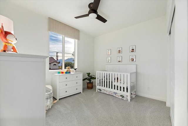 carpeted bedroom featuring ceiling fan and a nursery area