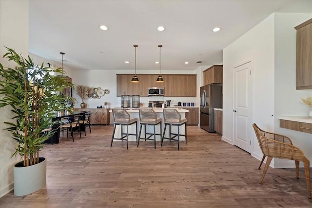 kitchen with hardwood / wood-style floors, a center island, a breakfast bar, pendant lighting, and appliances with stainless steel finishes