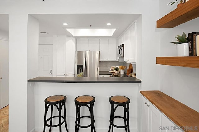 kitchen with kitchen peninsula, white cabinets, backsplash, and appliances with stainless steel finishes