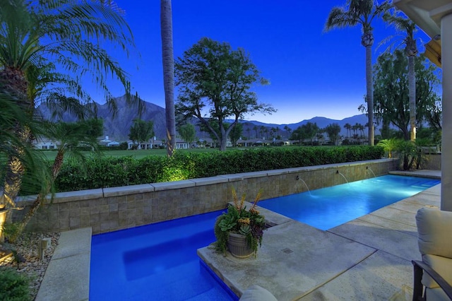 pool at dusk featuring pool water feature and a mountain view