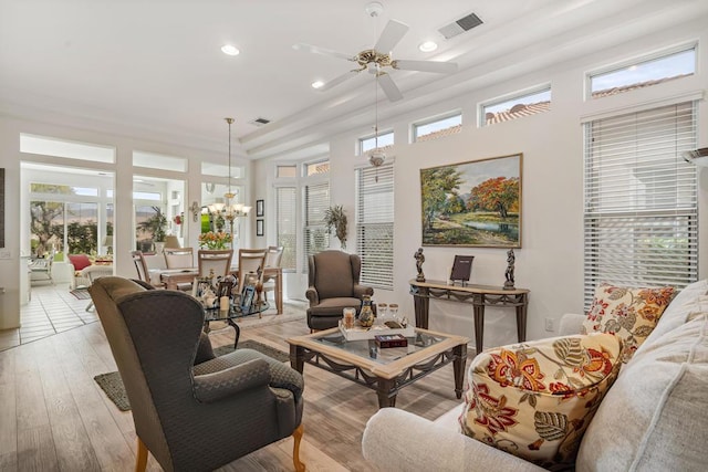 living room featuring ceiling fan with notable chandelier, light wood-type flooring, and a towering ceiling