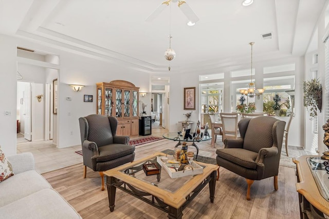 living room featuring a raised ceiling, light hardwood / wood-style floors, and ceiling fan with notable chandelier