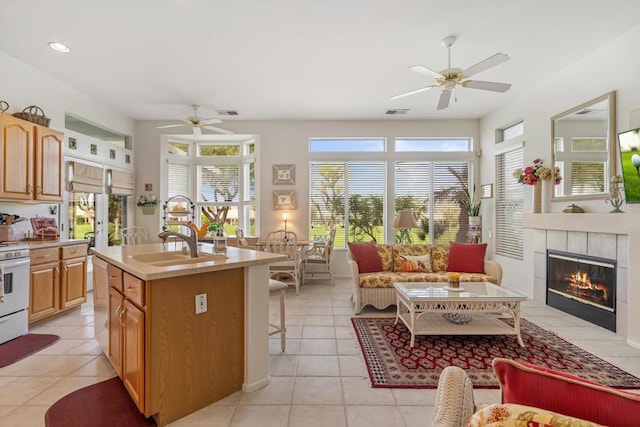 kitchen featuring a kitchen island with sink, a tile fireplace, sink, ceiling fan, and light tile patterned floors