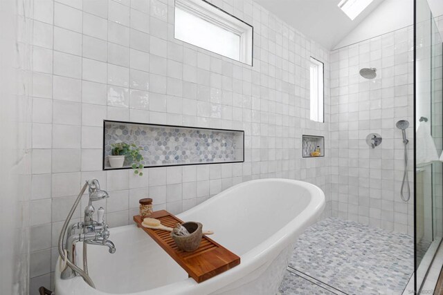 bathroom with shower with separate bathtub, lofted ceiling with skylight, and tile walls