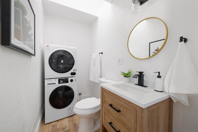 bathroom with toilet, stacked washer / drying machine, hardwood / wood-style flooring, and vanity