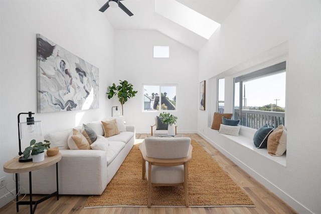 living room featuring ceiling fan, high vaulted ceiling, a skylight, and hardwood / wood-style floors