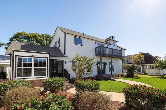 rear view of property featuring a lawn, french doors, and a balcony