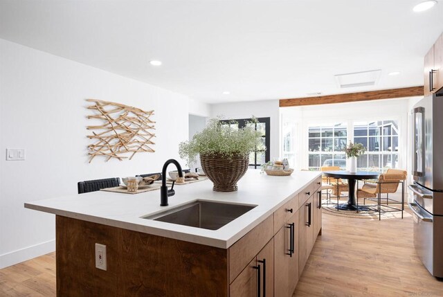 kitchen featuring stainless steel refrigerator, light wood-type flooring, sink, and a center island with sink