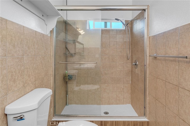 bathroom with toilet, tile walls, and a shower with shower door