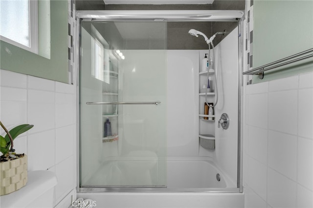 bathroom with combined bath / shower with glass door and tile walls