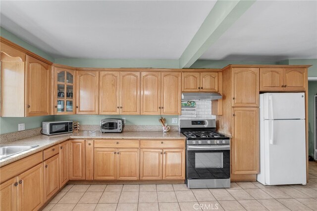 kitchen featuring light tile patterned floors, white refrigerator, beam ceiling, and stainless steel range with gas cooktop